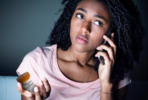 Young, black female on a cell phone talking to ESC's online pharmacy experts while holding medication bottle
